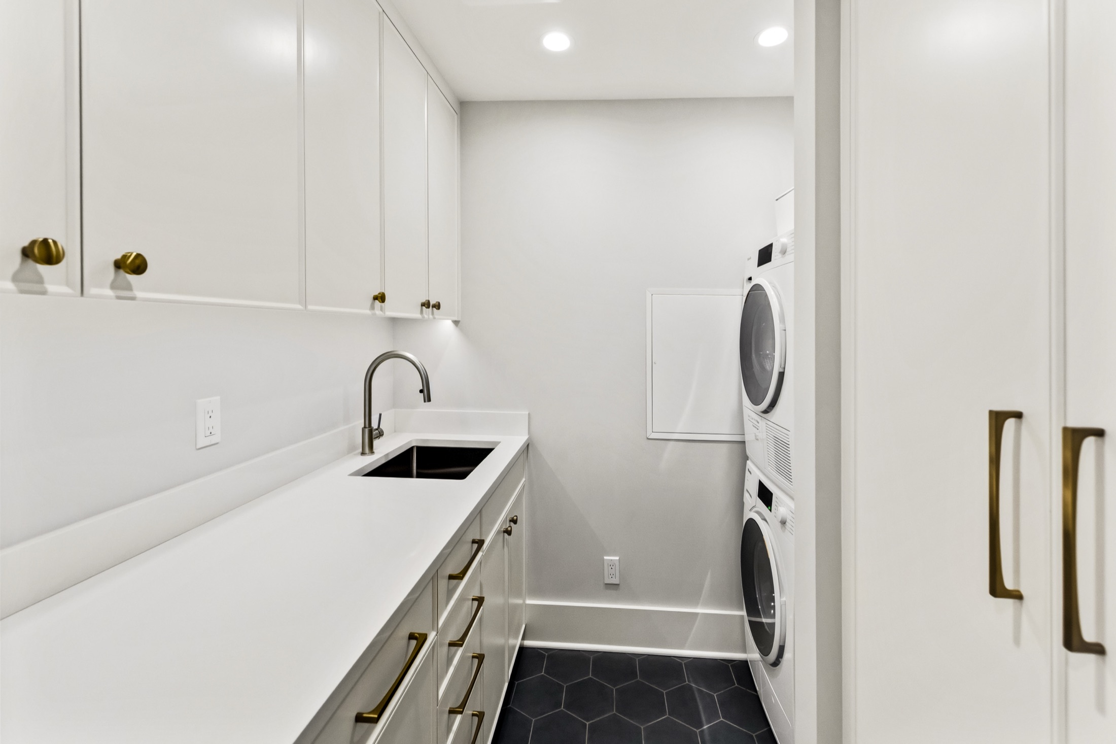 Tangletown laundry room with white cabinetry, utility sink, and stacked appliances